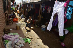 Child running down an alley. Woman washing clothes in a plastic bucket. Life in the back alleys of the Degüi Ayoreo community, outside Santa Cruz. In Santa Cruz, a city of nearly three million people, the Ayoreo Indians have become an example of how urban sprawl can devour a culture, making it invisible and stigmatising and endangering it, said anthropologist Luca Citarella. Credit: Miguel Ángel Souza/IPS