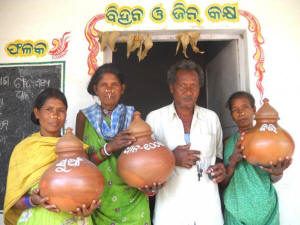 Traditional paddy seeds are labelled and stored in earthen pots at the Tentulipar community gene-seed-grain bank Picture of three women and one man holding jars containing traditional seeds.. Photo: Manipadma Jena/IPS &nbsp;