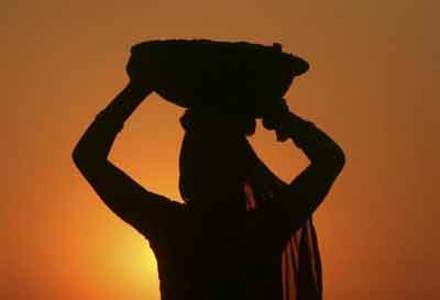 A woman laborer carrying cement is silhouetted against the setting sun at the site of a commercial complex on the outskirts of Jammu November 22, 2012. Photo: Reuters/Mukesh Gupta